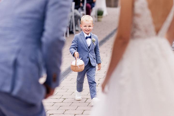 Kleiner Junge im eleganten Anzug bringt dem Brautpaar die Ringe während der freien Trauung in der Oase Weil, lächelnd und mit einem Körbchen in der Hand.